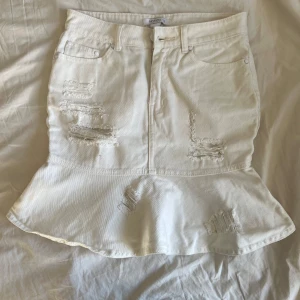 Vit jeanskjol med volang och slitningar  - Säljer en trendig vit jeanskjol med volang nertill och slitna detaljer framtill och baktill. Kjolen har klassiska jeansfickor. Perfekt inför sommaren!🤍