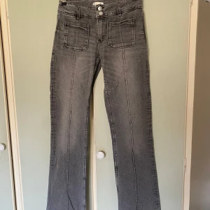 Grå jeans från Gina Tricot - Säljer ett par grå bootcut jeans från Gina Tricot med framfickor. Byxorna har låg midja och stängs med dragkedja och dubbla knappar. Perfekta för dig som gillar en klassisk och enkel stil.