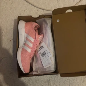 Adidas rosa sneakers med vita ränder - Säljer ett par snygga rosa Adidas sneakers med klassiska vita ränder på sidorna. Skorna har vit sula, rosa snörning och är tillverkade i ett ventilerande syntetmaterial. Perfekta för dig som vill ha en sportig och fräsch look.