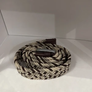 Beige och brunt flätat bälte från ONEWEAR Sweden - Snyggt flätat bälte i beige och brunt från ONEWear Sweden. Bältet har detaljer i brunt skinn och ett klassiskt spänne i silverfärg. Perfekt accessoar för att lyfta din outfit.