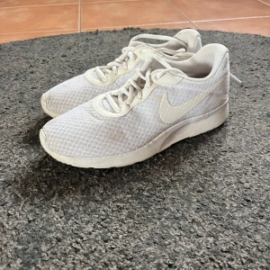 Vita sneakers från Nike - Säljer ett par vita sneakers från Nike med mesh-ovandel och klassisk swoosh på sidan. Skorna har snörning, perfekt för vardagsbruk eller lätt träning. Lätta och luftiga med sportig look. Det är lite missfärgning vid tårna men annars är de i fint skick o knappt använda