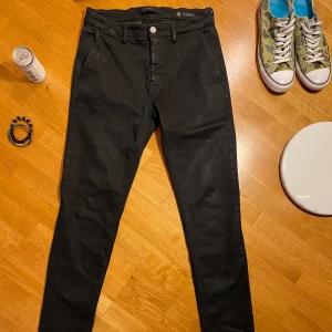 Svarta jeans Replay - Säljer ett par svarta byxor från Replay, modell Zeumar. Byxorna har en slim passform och klassisk design med dragkedja och knapp framtill. Perfekta för dig som gillar stilrena och bekväma jeans