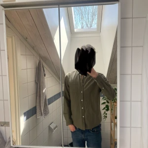 Olivgrön skjorta från Kappahl - Säljer en olivgrön skjorta från Kappahl med klassisk krage och vita knappar. Skjortan har lång ärm och är i ett mjukt bomullsmaterial. Perfekt för dig som gillar en enkel och stilren look.