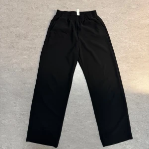 Svarta vida byxor från MNG - Svarta byxor från MNG med bred resår i midjan och raka, vida ben. Byxorna har en enkel och stilren design, perfekta för en avslappnad look. Tillverkade i ett mjukt och lätt material som passar perfekt till en sommardag