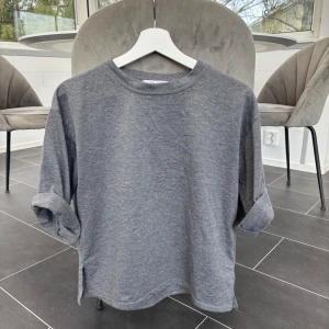 Mörkgrå basic tröja - En enkel och stilren mörkgrå tröja med rund halsringning och korta ärmar som man kan vika upp/ner. Tröjan har en avslappnad passform och är tillverkad i mjukt bomullsmaterial. Perfekt för en chill vardagslook!