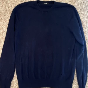 Marinblå cashmere tröja  - En klassisk marinblå cashmere tröja med rund halsringning och långa ärmar. Tröjan har ribbade muddar vid ärmslut och nederkant, vilket ger en snygg och tidlös look. Perfekt för lager-på-lager under kyliga dagar.