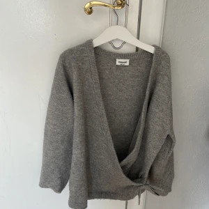 Grå omlottkofta från Kappahl - Mysig grå omlottkofta från Kappahl med djup v-ringning. Koftan är stickad och har långa ärmar, perfekt för lager-på-lager under kyliga dagar. Enkel och stilren design som passar till mycket.