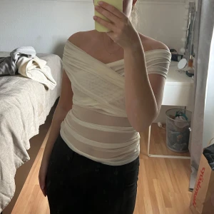 Vit offshoulder topp med omlott - Säljer en vit, tight offshoulder topp med omlott-design och transparenta partier. Ny utan prislapp. 