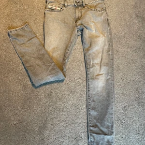 Grå jeansbyxor från Diesel Industry - Säljer ett par grå jeansbyxor från Diesel Industry med klassisk femficksdesign och raka ben. Byxorna har diskreta slitningar och logotypdetalj vid fickan. Perfekta för en avslappnad och stilren look.