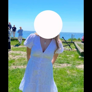 Vit kort klänning med broderade detaljer - Superfin vit klänning med v-ringning, puffärmar och broderade blommor. Klänningen har knappar framtill och volang nertill, samt är tillverkad i bomull. Perfekt för sommarens tillfällen och student. De är inte exakt den klänningen på sista bilden utan skillnaden är att min har en volang längst ner!(kolla bild 1) Endast använd en gång på min konfirmation. Pris kan alltid diskuteras💕💕