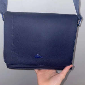 Lacoste  väska - Lacoste väska. Väldigt sällsynt. Finns inte att köpa längre, får plats med väldigt mycke utrymme. 3 fickor 