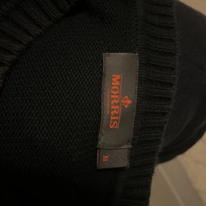 Marinblå stickad tröja från Morris - Säljer en marinblå stickad tröja från Morris med gul broderad logga på bröstet. Tröjan har rund halsringning och långa ärmar. Klassisk och stilren modell som passar perfekt till många tillfällen.