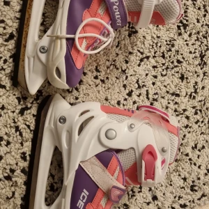 Vita och lila skridskor med rosa detaljer - Säljer ett par vita skridskor med lila och rosa detaljer från Ice Power. De har snörning och spänne för extra bra passform. Perfekta för vinterns skridskoåkning och finns i originalkartong.