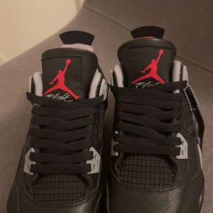 Nike Air Jordan 4 Retro Black/Red - Säljer ett par Nike Air Jordan 4 Retro i svart med röda och grå detaljer. Skorna har klassisk snörning, meshpaneler och tydlig Jumpman-logga på plösen. De är äkta nypris va ungefär 10 000kr och de är äkta. Skorna är helt oanvända då jag fick dom i present och de är tyvärr försmå