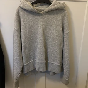 Grå hoodie i mjuk bomull - Säljer en enkel och stilren grå hoodie med huva och långa ärmar. Tröjan är i mjukt bomullsmaterial och har en avslappnad passform. Perfekt för chill dagar eller när du vill vara bekväm.