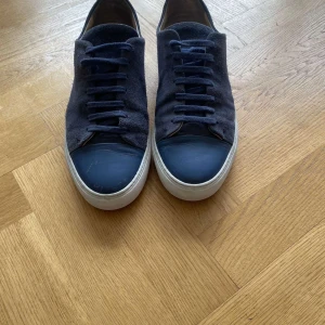 Mörkblå sneakers från Axel Arigato - Snygga mörkblå sneakers från Axel Arigato med ovandel i mocka och tåparti i slätare material. Skorna har vita platta sulor och matchande mörkblå snörning. Perfekta för dig som gillar stilrena och trendiga sneakers med premiumkänsla.