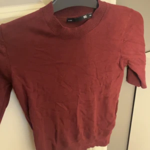 Vinröd tröja från 157, storlek XS - Vinröd tröja från 157 i storlek XS. Klassisk rund halsringning med ribbade detaljer vid kragen. Enkel och stilren design som passar perfekt till jeans eller kjol. Materialet känns mjukt och bekvämt mot huden.