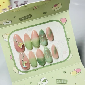 Grönrosa ombre lösnaglar med dekoration - Säljer ett set med långa, mandelformade lösnaglar i grön och rosa ombre. Några naglar har 3D-dekorationer som fjäril, måne och små stenar för extra bling. Naglarna har en glansig finish och kommer i söt förpackning. Perfekt för dig som vill ha unika och trendiga naglar.