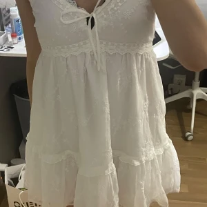 Vit kort sommarklänning från Hollister - Supersör vit sommarklänning köpt från Hollister. Har aldrig använt den och prislappen finns kvar. Den har en massa detaljer, till exempel blommor och spets. Passar perfekt till sommaren!! Köpte den för ungefär 600kr men säljer den för bara 450kr
