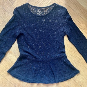 Svart spetspeplum från Only, Jacqueline de Yong - Supersnygg svart peplumtop från Only, Jacqueline de Yong, i genombruten spets med lång ärm. Toppen har rund halsringning och markerad midja som ger en feminin siluett. Perfekt när du vill sticka ut lite extra med cool spetsdetalj.