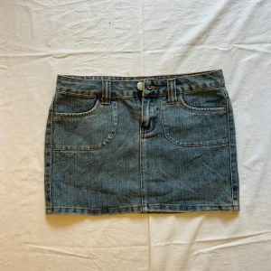 Klassisk jeanskjol i blå denim - Midjemått rakt över: 38 cm, längd: 33 cm Säljer en klassisk blå jeanskjol i kort modell med låg midja. Kjolen har två stora fickor fram och två bakfickor med lock och knapp. Snygga sömmar och bälteshällor ger en tidlös look. Perfekt till sneakers eller boots för en chill vibe.
