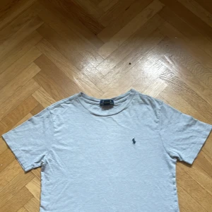 Ljusgrå t-shirt från Polo Ralph Lauren - En stilren ljusgrå t-shirt från Polo Ralph Lauren med klassisk passform och korta ärmar. T-shirten har en liten broderad logga på bröstet och är gjord i mjuk bomull. Perfekt till jeans eller shorts för en clean look. Storlek 10-12 år!!!