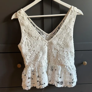 Vit spetsig linnetopp från Zara - Superfin vit linnetopp från Zara med v-ringning och breda axelband. Toppen har ett detaljerat spetsmönster och volang nertill som ger en romantisk vibe. Perfekt för varma dagar eller när du vill känna dig extra söt.