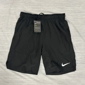 Svarta Nike träningsshorts S - Svarta träningsshorts från Nike med vit logga på benet och elastisk midja med snörning. Tillverkade i lätt och snabbtorkande material med Dri-Fit-teknologi. Perfekta för gymmet eller löprundan, riktigt sköna och stilrena.