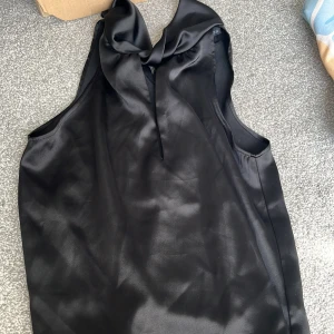 Svart ärmlös sidenblus från Zara  - Supersnygg svart blus i glansigt sidenmaterial med ärmlös design och en elegant rosettdetalj vid halsen. 