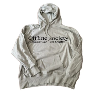 Ljusgrå hoodie Offline Society H&M - Ljusgrå hoodie från H&M med trycket 'Offline Society Members' club Los Angeles' på bröstet. Tröjan har huva med snörning, känguruficka och relaxed fit. Perfekt för en chill och avslappnad stil.