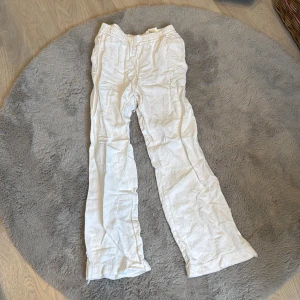Vita linnebyxor med resårmidja XS - Snygga och luftiga vita linnebyxor i blandmaterial med resår i midjan och avslappnad passform. Perfekta för varma dagar när du vill ha något bekvämt och stilrent. Byxorna har raka ben och dragsko i midjan för extra komfort.