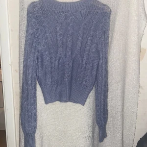 Ljuslila stickad tröja från Clockhouse - Superfin ljuslila stickad tröja från Clockhouse med flätstickat mönster och bred ribbad mudd i midjan och vid ärmslut. Tröjan har en klassisk rund halsringning och långa ärmar, perfekt för lager på lager under kyliga dagar.