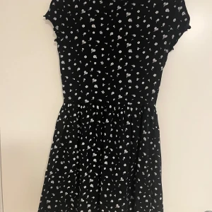 Svart blommig klänning FB Sister XS - Supersöt svart kortklänning från FB Sister i storlek XS. Klänningen har små vita blommor över hela tyget, rund hals och korta ärmar. Den har en lätt utställd kjol och är perfekt för dig som gillar en feminin och chill stil.
