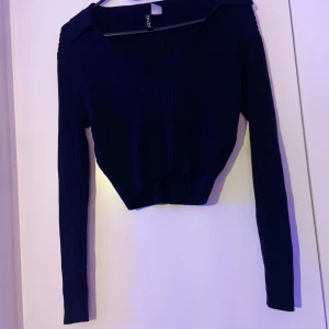 Svart ribbad croppad stickad tröja Divided - Säljer en svart croppad stickad tröja från Divided. Tröjan har v-ringning, krage och långa ärmar. Ribbad struktur ger en snygg och trendig look, perfekt till jeans eller kjol. Enkel att styla och superbekväm.