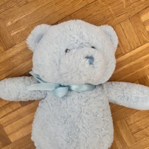 Nallebjörn  - Bilderna visar en ljusblå nallebjörn med rosett runt halsen. Ingen bok syns på bilderna, endast en mjuk leksak. Ingen information om titel, författare eller bokinnehåll kan utläsas.