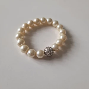 Pärlarmband med glittrig detalj - Sött armband med stora vita pärlor och en glittrig silverfärgad kula som extra detalj. Perfekt accessoar för dig som vill ha något klassiskt men ändå med lite bling.
