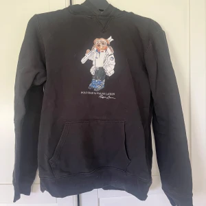 Svart hoodie Polo Ralph Lauren XL - Svart hoodie från Polo Ralph Lauren i storlek XL (barn) fint skick men har ett litet hål på armbågen men inget som syns (se bild). 