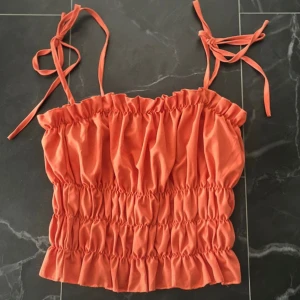 Volang topp - Orange topp med volanger. Axelbanden går att knyta, den är aldrig använd! Passar strl S.