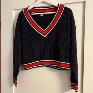 Svart ribbad v-ringad tröja med ränder - Svart ribbstickad tröja med v-ringning och snygga röda och vita ränder vid hals, ärmslut och nederkant. Croppad modell med lång ärm.