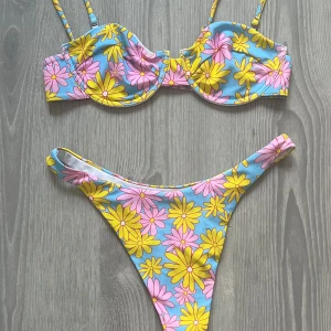Blommig bikini i pastellfärger - Superfin bikini med blommigt mönster i gult och rosa på ljusblå botten. Överdelen har bygel och smala axelband, underdelen är högt skuren. Perfekt för stranden eller poolen, ger en färgglad och retro vibe.