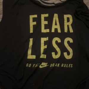 Svart Nike t-shirt med tryck - Svart t-shirt från Nike med stort gult FEARLESS-tryck och texten 'GO FAST BRAK RULES' på framsidan. Slim fit-modell med korta ärmar och rund hals. Perfekt för dig som gillar sportig och cool stil.