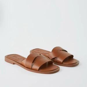 Bruna sandaler i skinn med korsade remmar - Snygga bruna sandaler från Zara med korsade remmar i skinn. Platt sula och öppen tå ger en clean och stilren look, perfekt för varma dagar. Enkla att matcha med allt i garderoben.