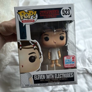 Stranger Things: Eleven (With Electrodes) #523 - Cool Funko Pop! vinylfigur av Eleven från Stranger Things, med elektroder och sjukhusklänning. Perfekt för fans av serien och samlare som vill ha något unikt från Netflix-världen. Limited Fall Convention Exclusive! Pris kan diskuteras!