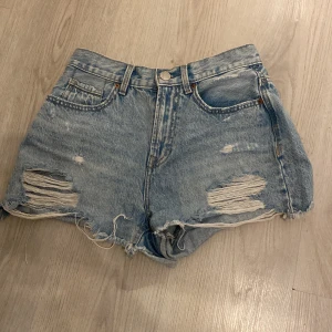 Blåa jeansshorts Vero Moda - Snygga ljusblå jeansshorts från Vero Moda med slitna detaljer framtill. Klassisk femficksmodell med råa kanter och avslappnad passform. Perfekta för sommardagar och festivalhäng.