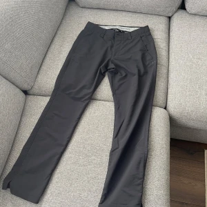 Under armour byxor  - Svarta byxor från Under Armour med raka ben och diskret logga vid fickan. Byxorna har bälteshällor, fram- och bakfickor samt är tillverkade i ett stretchigt syntetmaterial som känns sportigt och bekvämt.