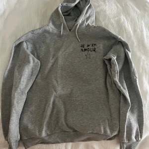 Grå hoodie ”Je m’en amour” och stjärna, tryck på ryggen Gina Tricot - Grå hoodie med huva och snörning, samt svart broderad text 'JE M'EN AMOUR' och en liten stjärna på bröstet från Gina Tricot. En tröja i storlek 158/164 som inte passar längre 🥰 Tryck på baksidan också!