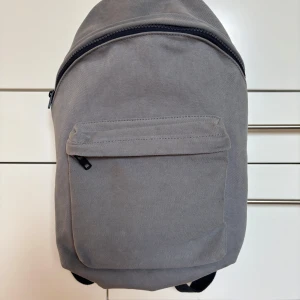 Grå ryggsäck från Brandy Melville/ John Galt Switzerland i perfekt skick  - Säljer en stilren grå ryggsäck från Brandy Melville/ John Galt Switzerland i klassisk design. Väskan har ett stort huvudfack, en praktisk ytterficka med dragkedja och justerbara marinblå axelremmar. Materialet är slitstark bomull och detaljer i läder upptill. Fodrad med marinblå galon så vattentät! Perfekt skick!