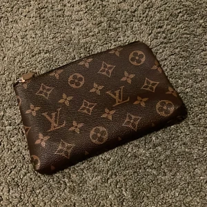 monogram kuvertväska med mönster  - Säljer en unik brun kuvertväska med mönster och ikoniskt monogrammönster i guldiga toner! Väskan är i skinn och har dragkedja upptill, Perfekt storlek för det viktigaste och en snygg detalj till din outfit samt otroligt bra skick och pris 🏆 