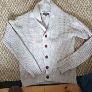 Ljusgrå kofta från Carter & Rise - Säljer en ljusgrå stickad kofta från Carter & Rise med snygg sjalkrage och fem mörka knappar framtill. Koftan har långärmad design och breda ribbade muddar vid ärmslut och nederkant. Perfekt för lager-på-lager och chill vibes.