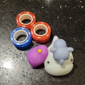 3 Magnetic Fidget Rings + 3 Squishy Toys - Tre Magnetiska Ringar, två i rosa och en i blått med glittrig finish. Ringarna är runda och har en cool, modern vibe. Perfekta för att hålla händerna sysselsatta och få tiden att gå! + Tre Squishy Toys, en ljusblå Val/Haj, en blå elefant och en lila pingvin. Bra skick och fastnar på väggen!! 